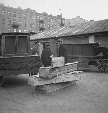 archiwalne fotogr... - Jewish undertakers converse next to a pile of wooden coffins in the Warsaw ghetto.jpg